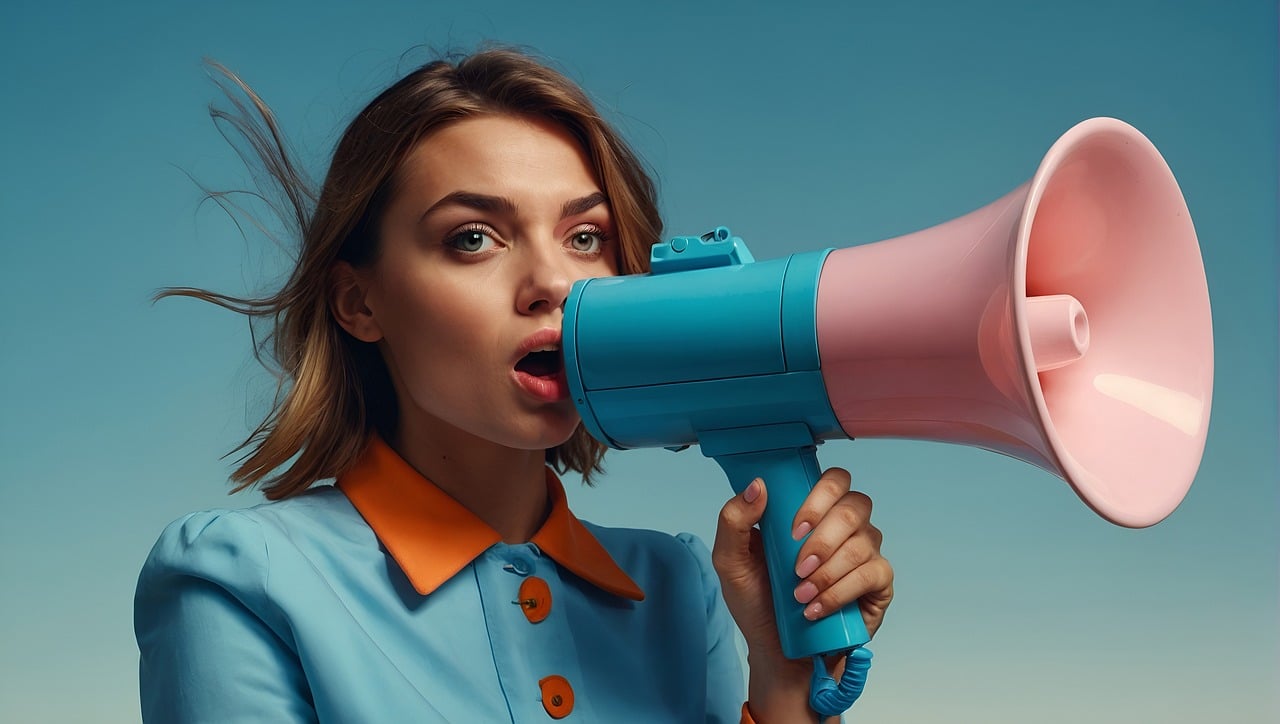 Influencer giovane con camicia azzurra che parla attraverso un megafono rosa e blu, su sfondo neutro.