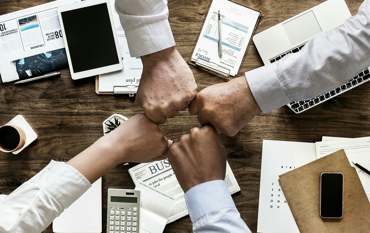 Mani di un team che si uniscono per un gesto di collaborazione su una scrivania, simbolo di comunicazione interna efficace in un contesto aziendale